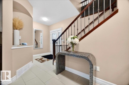 Entryway featuring light-toned tile flooring and a grand staircase with dark wood handrails and decorative balusters - 1326 Cunningham Drive, Edmonton, AB 