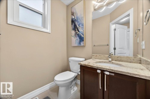 Powder room featuring a corner vanity with a stone countertop, an integrated sink, and dark wood cabinetry - 1326 Cunningham Drive, Edmonton, AB 