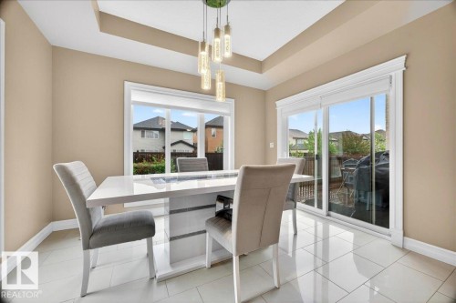 Dining area featuring a contemporary chandelier, tray ceiling, and light tile flooring - 1326 Cunningham Drive, Edmonton, AB 