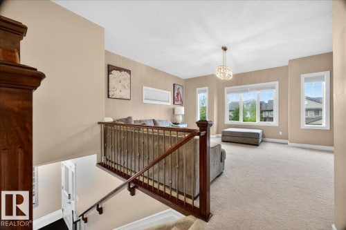 Upper-level living area featuring neutral carpeting, abundant natural light from multiple windows, and a decorative chandelier - 1326 Cunningham Drive, Edmonton, AB 