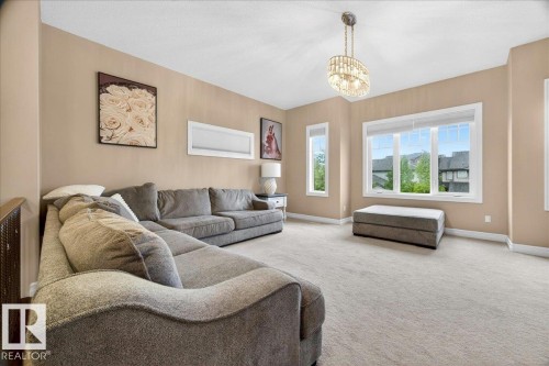 Carpeted living area featuring a large picture window, two vertical windows, a built-in chandelier, and neutral wall tones - 1326 Cunningham Drive, Edmonton, AB 
