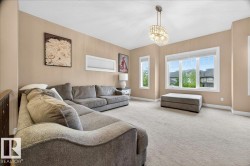 Carpeted living area featuring a large picture window, two vertical windows, a built-in chandelier, and neutral wall tones - 