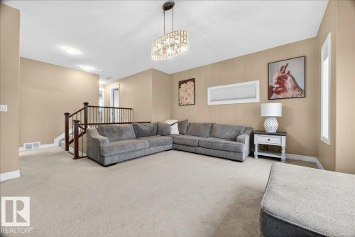 Carpeted living area featuring neutral-toned walls, a crystal chandelier, and a wood-toned staircase railing with white balusters - 1326 Cunningham Drive, Edmonton, AB 