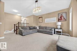 Carpeted living area featuring neutral-toned walls, a crystal chandelier, and a wood-toned staircase railing with white balusters - 