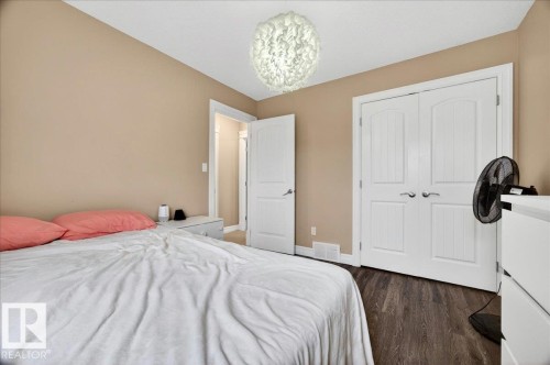 Bedroom featuring wood-finish flooring, neutral wall paint, white trim, a decorative ceiling light fixture, and white double-panel closet doors - 1326 Cunningham Drive, Edmonton, AB 
