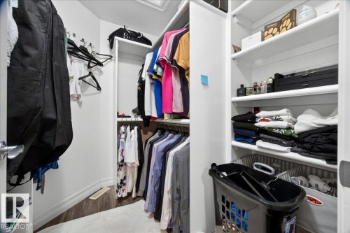 Walk-in closet featuring white built-in shelving, multiple hanging rods, corner shelving, and wood-finish flooring - 1326 Cunningham Drive, Edmonton, AB 