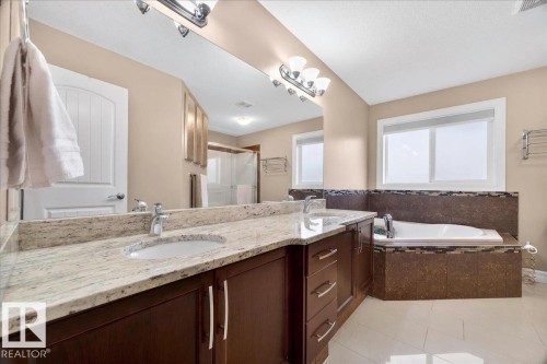 Double vanity with stone countertop and undermount sinks, wood-finish cabinetry, built-in soaking tub, and tile flooring - 1326 Cunningham Drive, Edmonton, AB 
