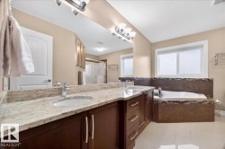 Double vanity with stone countertop and undermount sinks, wood-finish cabinetry, built-in soaking tub, and tile flooring - 