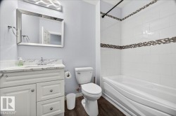 Bathroom featuring a white vanity with marble-look countertop, rectangular mirror, wood-finish flooring, and a tiled shower-tub combination with mosaic accent band - 