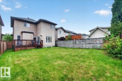 Expansive backyard featuring a wood deck with lattice skirting, a manicured lawn, and perimeter fencing - 