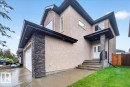 Stucco exterior featuring stacked stone accents, a covered entry with a stone-clad column, and a double garage with a white door - 1326 Cunningham Drive, Edmonton, AB 