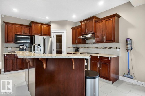 Kitchen featuring rich wood cabinetry, stainless steel appliances, a center island with bar seating, light-toned countertops, and tile flooring - 1326 Cunningham Drive, Edmonton, AB 