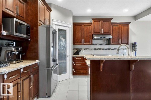 Kitchen featuring rich wood cabinetry, stainless steel appliances, granite-look countertops, and a mosaic tile backsplash - 1326 Cunningham Drive, Edmonton, AB 
