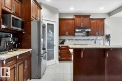 Kitchen featuring rich wood cabinetry, stainless steel appliances, granite-look countertops, and a mosaic tile backsplash - 