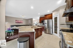 Spacious kitchen featuring light tile flooring, granite countertops, cherry-toned cabinetry, stainless steel appliances, and an integrated kitchen island with a sink - 