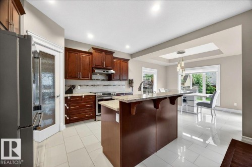 Kitchen featuring dark wood cabinetry, stainless steel appliances, a center island with countertop seating, and light tile flooring - 1326 Cunningham Drive, Edmonton, AB 