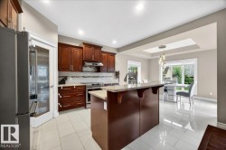 Kitchen featuring dark wood cabinetry, stainless steel appliances, a center island with countertop seating, and light tile flooring - 
