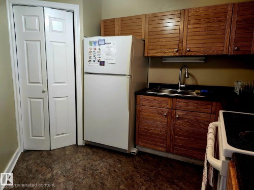 Kitchen area featuring wood-finish cabinetry, a stainless steel sink with a gooseneck faucet, dark countertops, and resilient flooring - 1600 10149 Saskatchewan Drive, Edmonton, AB 