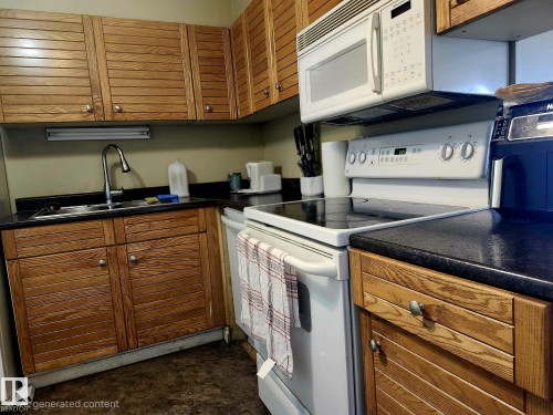 Kitchen featuring wood-finish cabinetry, dark countertops, a stainless steel sink with a gooseneck faucet, a built-in microwave, and an electric range - 1600 10149 Saskatchewan Drive, Edmonton, AB 