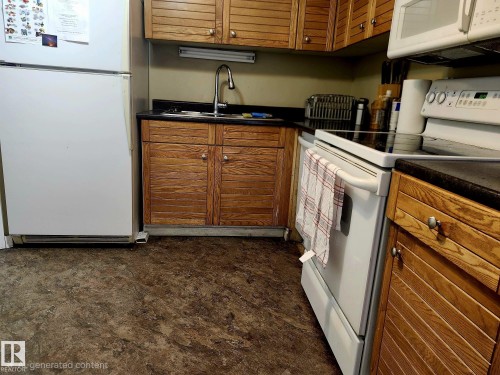 Kitchen featuring wood cabinetry with silver-tone hardware, dark countertops, a stainless steel sink with a gooseneck faucet, and resilient flooring - 1600 10149 Saskatchewan Drive, Edmonton, AB 