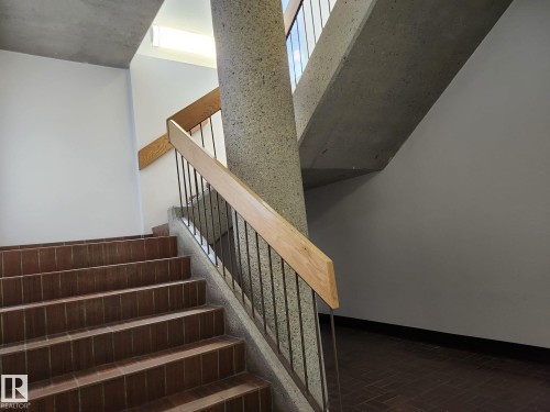 Stairwell featuring terra cotta tile treads, a concrete column, and a wood-finish handrail with metal balusters - 1600 10149 Saskatchewan Drive, Edmonton, AB 