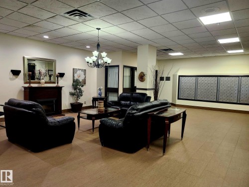 Lobby area featuring a fireplace with a wood mantel, a chandelier, and a large wall of mailboxes - 1600 10149 Saskatchewan Drive, Edmonton, AB 