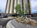 High-rise building with numerous balconies, featuring a stone-clad entrance, a rock garden with various plantings, and a paved circular driveway - 1600 10149 Saskatchewan Drive, Edmonton, AB 