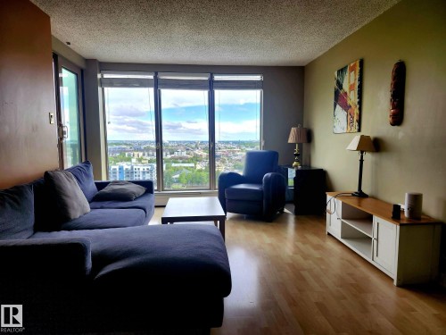 Spacious living area featuring expansive floor-to-ceiling windows, wood-finish flooring, and a sliding glass door - 1600 10149 Saskatchewan Drive, Edmonton, AB 