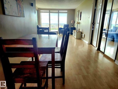 Light wood-finish flooring extends through this interior space, featuring a dining area with a dark wood table and chairs - 1600 10149 Saskatchewan Drive, Edmonton, AB 