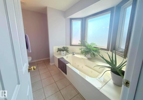 Soaking tub with integrated jets and tiled surround, set beneath a bay window with wood-frame windows. - 825 112B St, Edmonton, AB 
