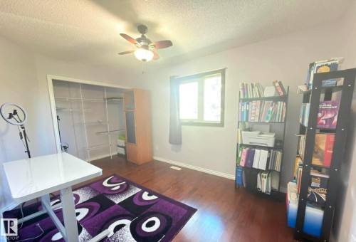 Spacious room featuring hardwood flooring, a ceiling fan with integrated lighting, and a window with dark trim. - 825 112B St, Edmonton, AB 
