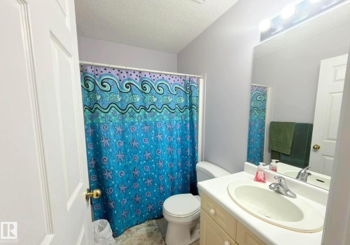 Bathroom featuring a single vanity with a white countertop and integrated sink, a large wall-mounted mirror, overhead bar lighting, and a toilet. - 825 112B St, Edmonton, AB 