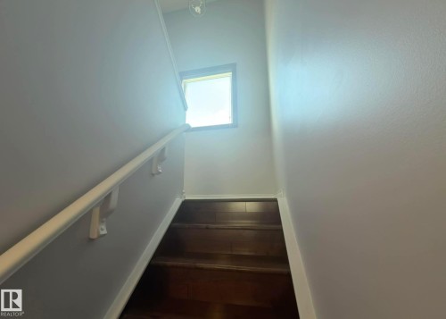 Stairway featuring wood-finish treads, a contrasting white handrail, and a high-set window providing natural illumination. - 825 112B St, Edmonton, AB 