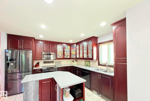 Kitchen featuring rich wood-finish cabinetry, stainless steel appliances, and a central island with a speckled countertop. - 825 112B St, Edmonton, AB 
