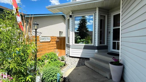 Exterior featuring light grey siding, a multi-pane bay window, and a white storm door. Two trees in the front garden will be removed. - 825 112B St, Edmonton, AB 