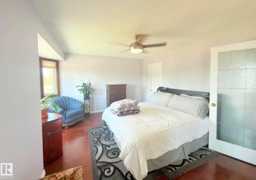 Spacious room featuring Hardwood flooring, a ceiling fan with integrated lighting, and a white paneled door and bay windows allowing natural lighting to brighten up the room. - 825 112B St, Edmonton, AB 