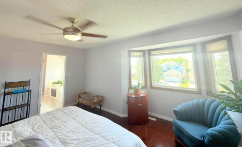 Hardwood-finish flooring featuring a multi-pane bay window, an overhead ceiling fan, and an open doorway revealing a tiled bathroom with a Whirlpool Jet Tub. - 825 112B St, Edmonton, AB 