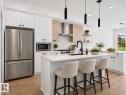 Modern kitchen featuring a central island with countertop seating, white cabinetry, and stainless steel appliances - 8108 230 Street, Edmonton, AB 
