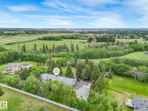 Expansive property featuring a central residence, mature evergreen trees, a detached garage, and a long gravel driveway - 11921 231 Street, Edmonton, AB 