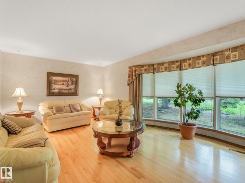 Spacious living area featuring light wood-finish flooring, a large bay window, window treatments, and textured wall finishes - 11921 231 Street, Edmonton, AB 