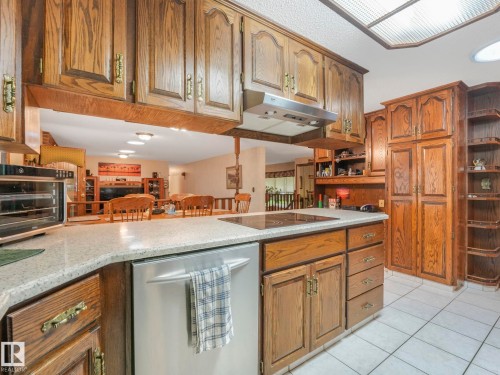 Kitchen featuring extensive wood cabinetry, light-toned countertops, integrated cooktop, stainless steel dishwasher, and tiled flooring - 11921 231 Street, Edmonton, AB 