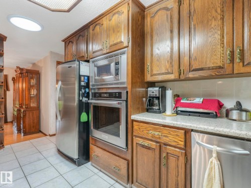 Kitchen featuring wood cabinetry, stainless steel appliances, a built-in oven and microwave, a white tile floor, and a skylight - 11921 231 Street, Edmonton, AB 