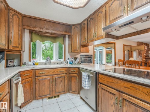 Kitchen featuring wood cabinetry, white tile flooring, stainless steel dishwasher, and a built-in cooktop - 11921 231 Street, Edmonton, AB 