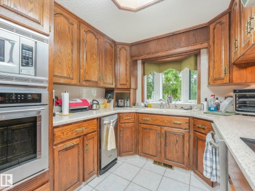 Kitchen featuring extensive wood cabinetry, light-toned countertops, and a built-in stainless steel microwave and oven - 11921 231 Street, Edmonton, AB 
