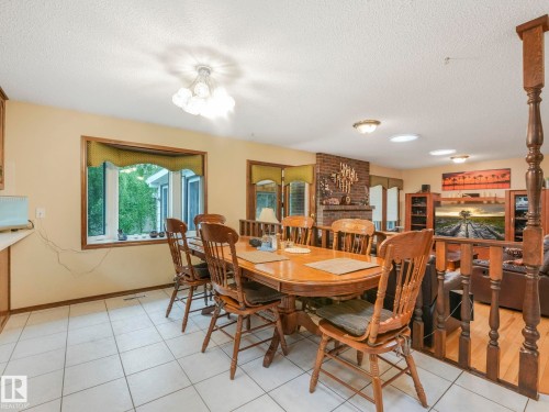 Dining area featuring white tile flooring, a large window, and a built-in brick fireplace - 11921 231 Street, Edmonton, AB 