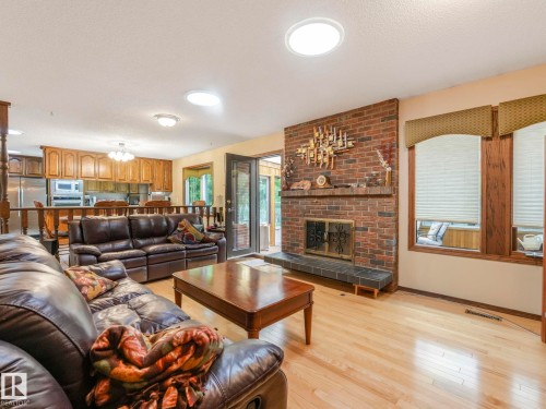 Living area featuring a brick fireplace with a slate hearth, light wood-finish flooring, and multiple windows with valances - 11921 231 Street, Edmonton, AB 