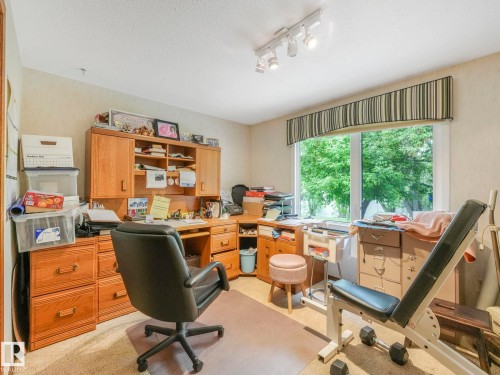 Room featuring a built-in wood-finish desk and cabinetry, a large window with a striped valance, track lighting, and textured wall covering - 11921 231 Street, Edmonton, AB 