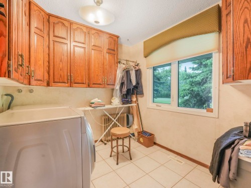 Utility room featuring wood cabinetry, a window with outdoor tree scenery, tile flooring, and a ceiling-mounted light fixture - 11921 231 Street, Edmonton, AB 