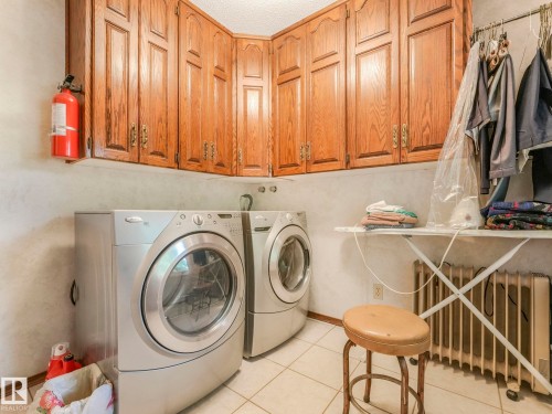 Laundry area featuring white tile flooring, natural wood cabinetry, and textured wall finishes - 11921 231 Street, Edmonton, AB 