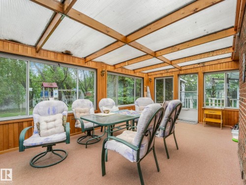 Enclosed sunroom featuring a transparent panel roof with wood beams, wood-paneled walls, multiple windows, and carpeting - 11921 231 Street, Edmonton, AB 